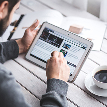 Person holding a tablet and reading, with coffee on a white wooden table.